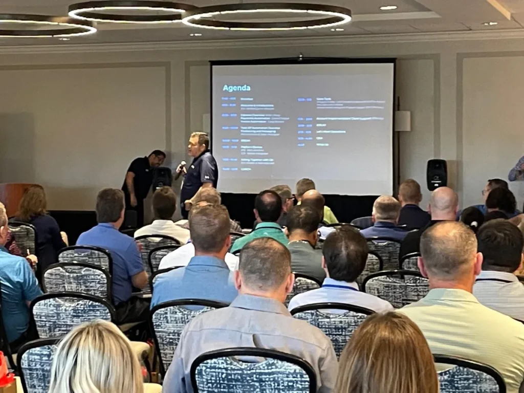 Conference speaker addressing audience with agenda slide displayed